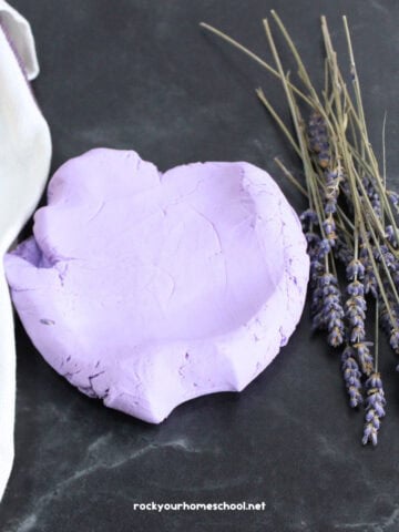 Example of easy lavender cloud dough recipe in the shape of a heart with lavender flowers and towel.