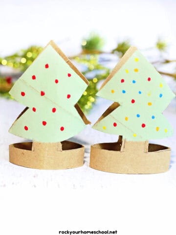 2 examples of Christmas tree toilet paper roll crafts painted light green with pine branches in background.