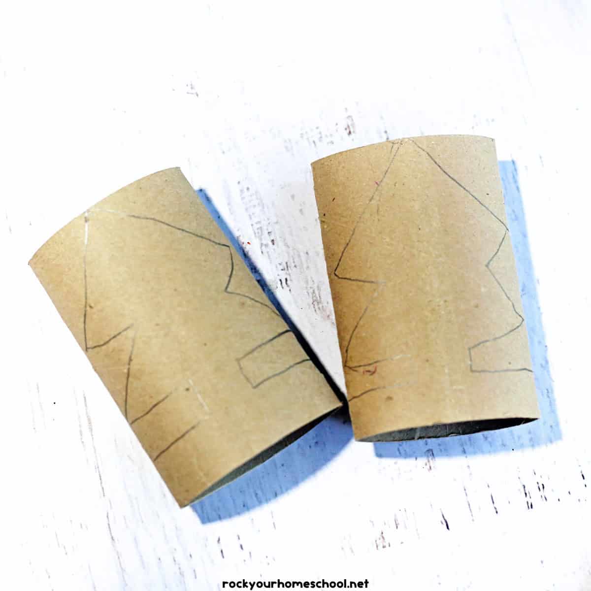 2 empty toilet paper rolls that are flattened and have a Christmas tree shape drawn on them with pencil.