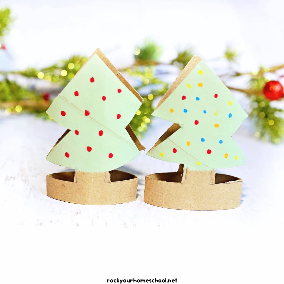 2 examples of Christmas tree toilet paper roll crafts painted light green with pine branches in background.