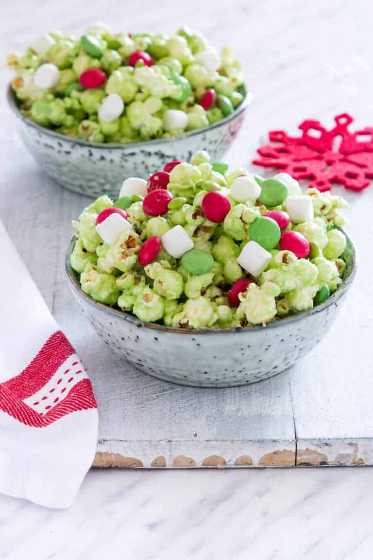 2 bowls of Grinch popcorn with chocolate candies and mini marshmallows.