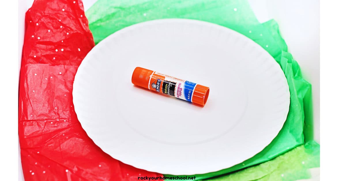 White paper plate, glue stick, and glitter tissue paper in red and green.