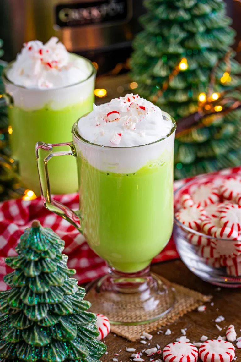 Two glass mugs of slow cooker Grinch hot cocoa with bowl of peppermint candies.