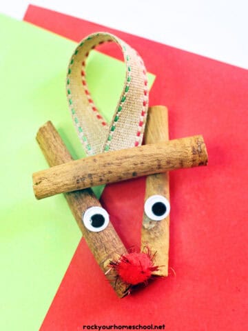 Example of cinnamon stick reindeer ornament craft with googly eyes, red pom pom, and ribbon.