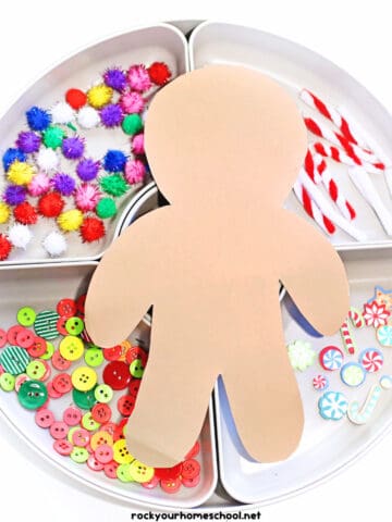 Gingerbread man cut-out with pom poms, pipe cleaners, buttons, and foam stickers on white tray.