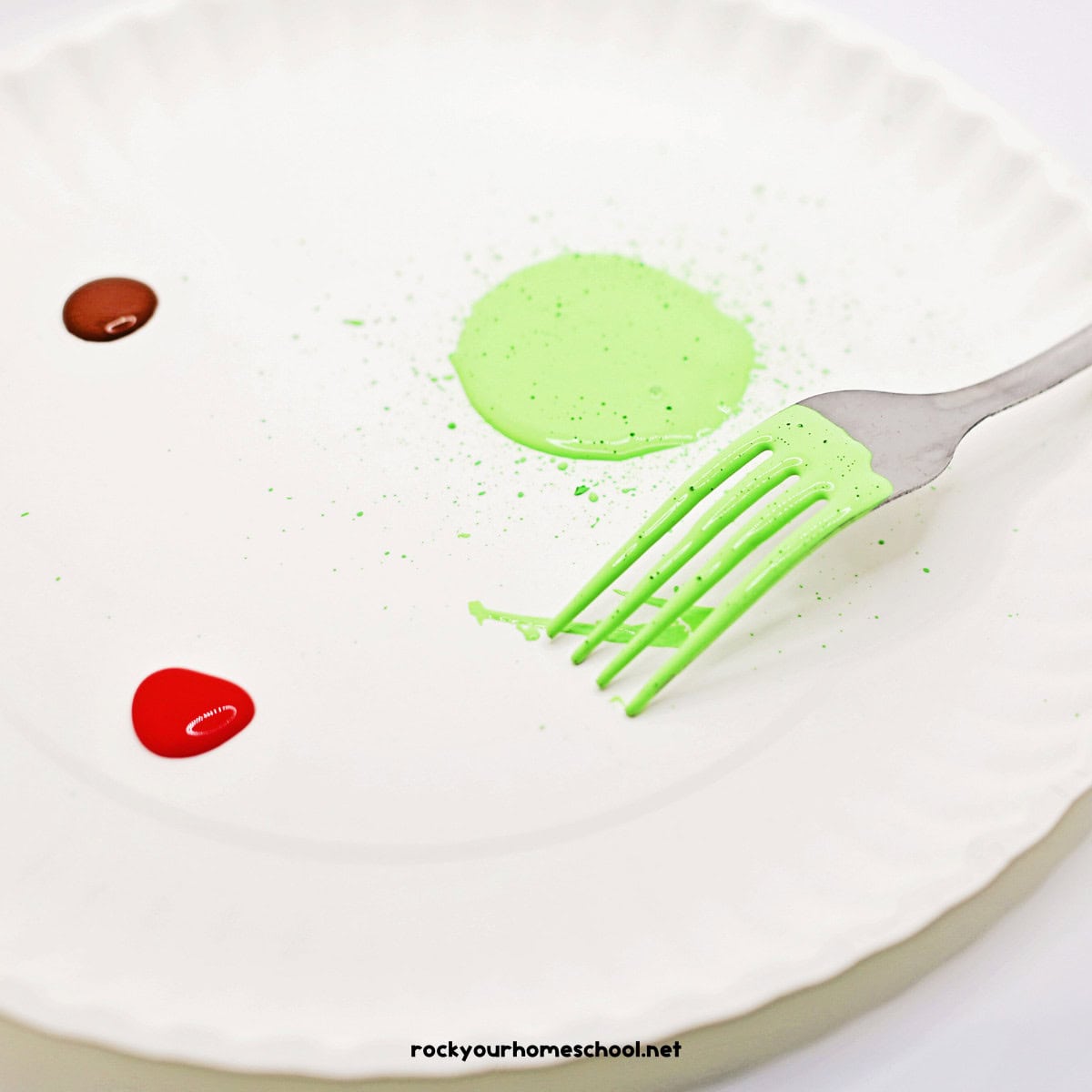 Paper plate with fork in light green paint and red and brown paint blobs.