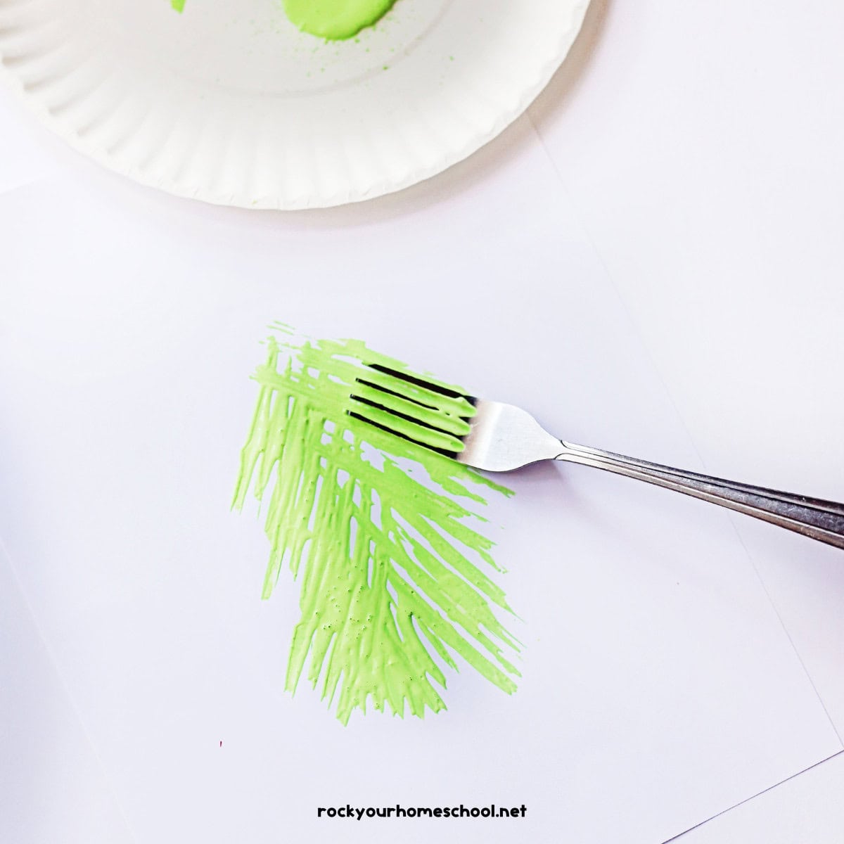 Fork with light green paint and paper plate.