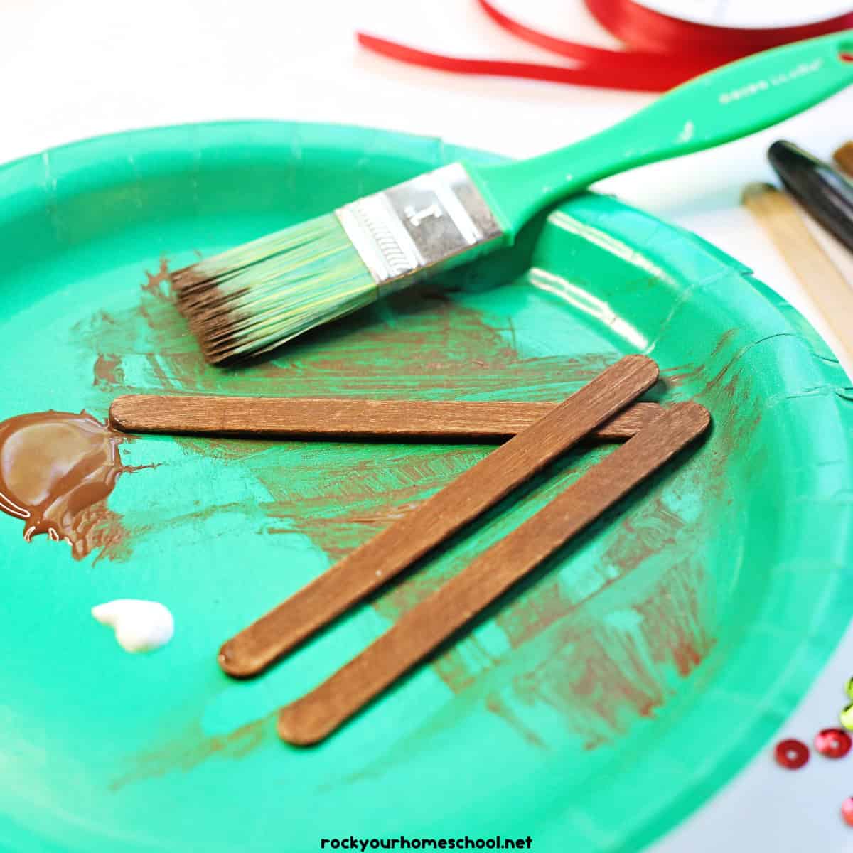 3 popsicle sticks painted brown with paint brush on green paper plate.