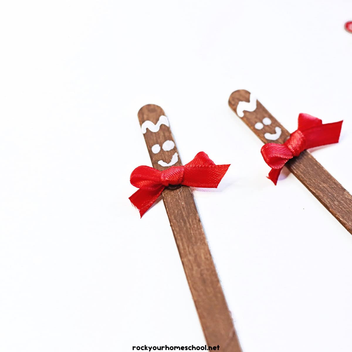 2 examples of brown popsicle sticks with small red bows and white paint smiley faces.