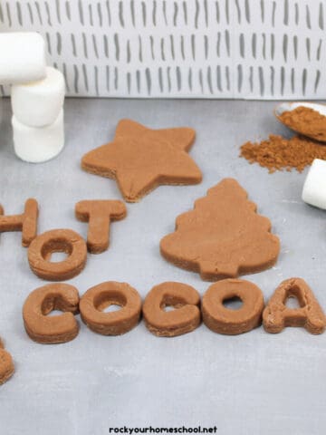 Hot chocolate playdough in star and Christmas tree with marshmallows and cocoa powder on spoon and H O T C O C O A.