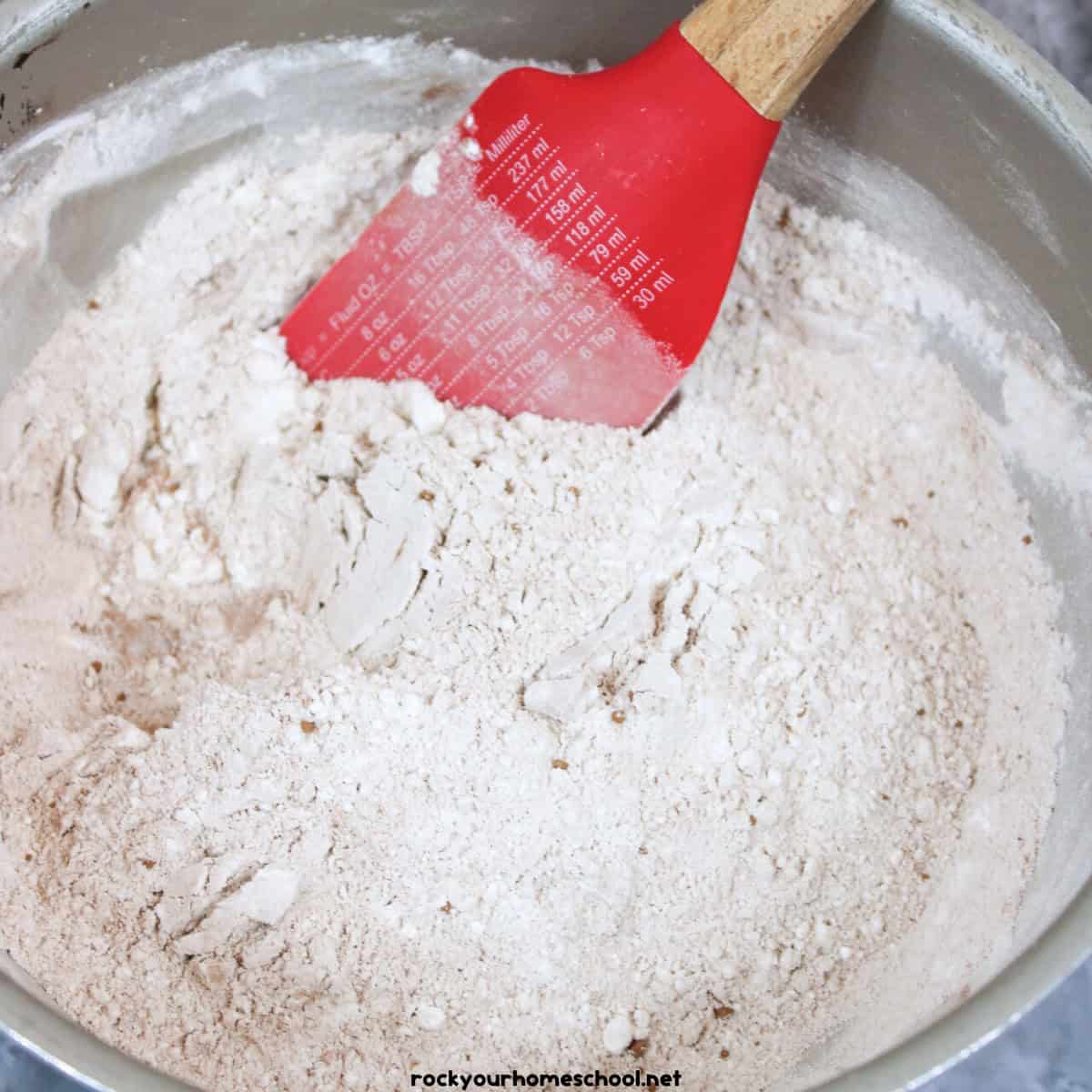 Mixing bowl with  dry ingredients of flour, cornstarch, cream of tartar, and cocoa powder and red spatula.