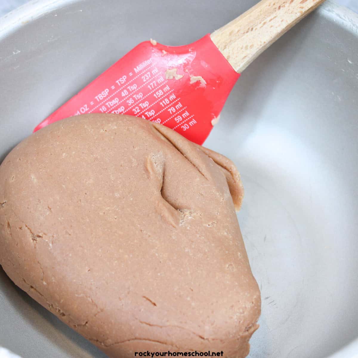 Ball of hot chocolate playdough in saucepan with red spatula.