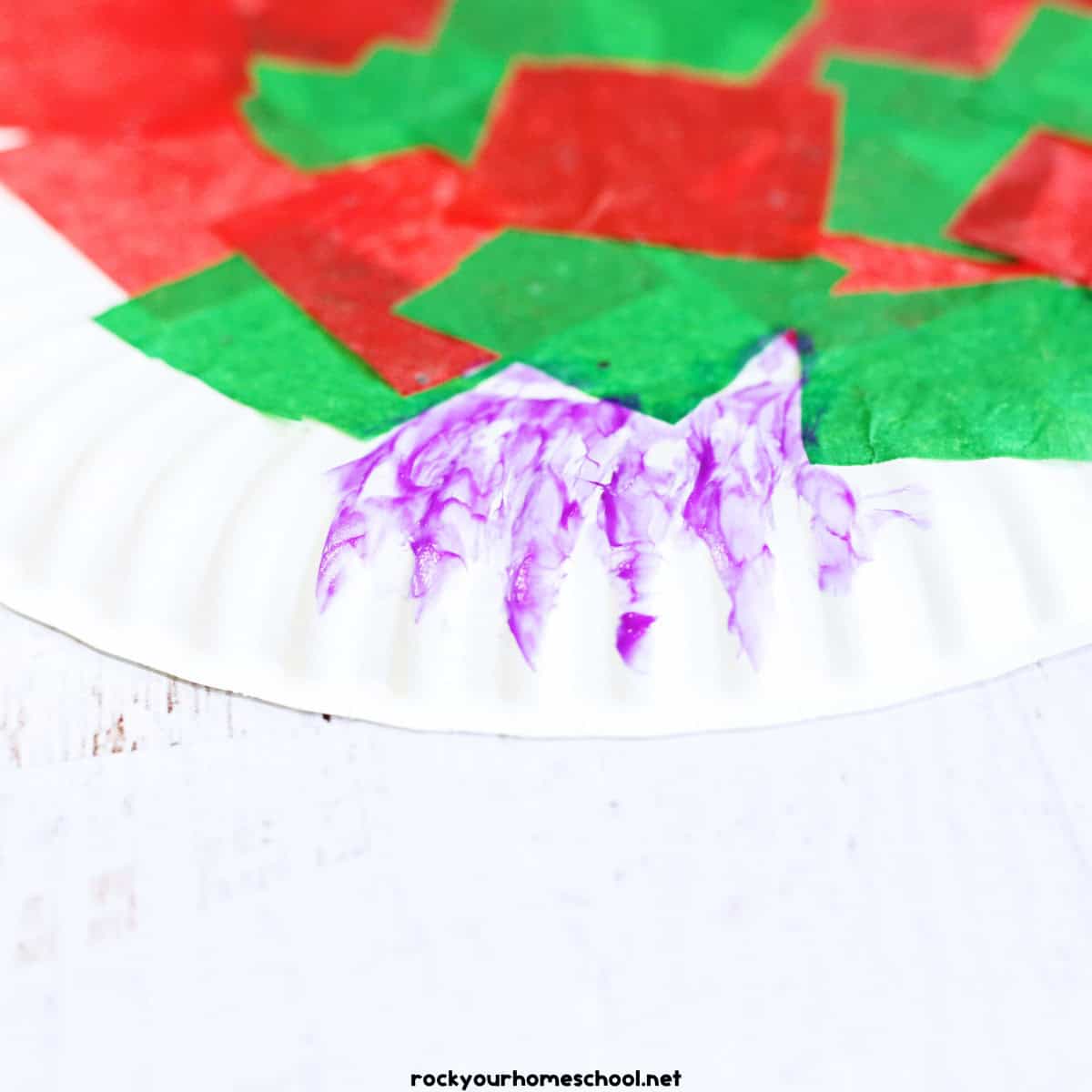 Purple glue stick on red and green tissue paper squares on white paper plate.