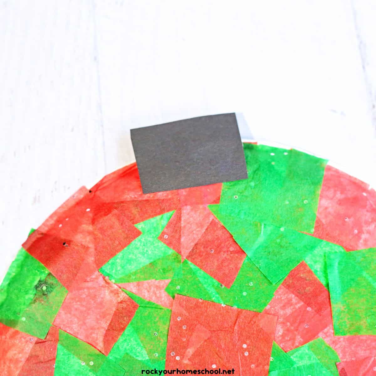 Black construction paper rectangle on paper plate with red and green sparkle tissue paper.