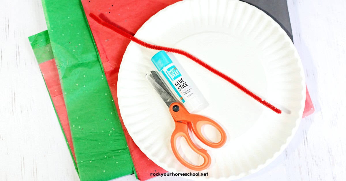 Green and red tissue paper, scissors, glue stick, red pipe cleaner, black construction paper, and paper plate.