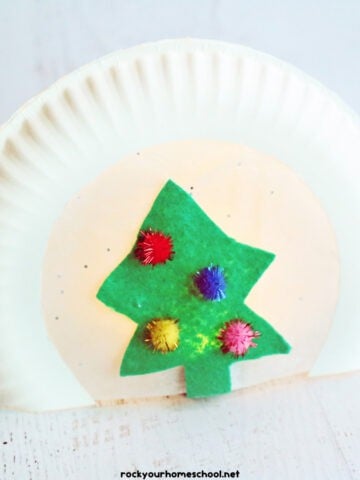 Christmas paper plate craft with green felt tree, pom poms, and light.