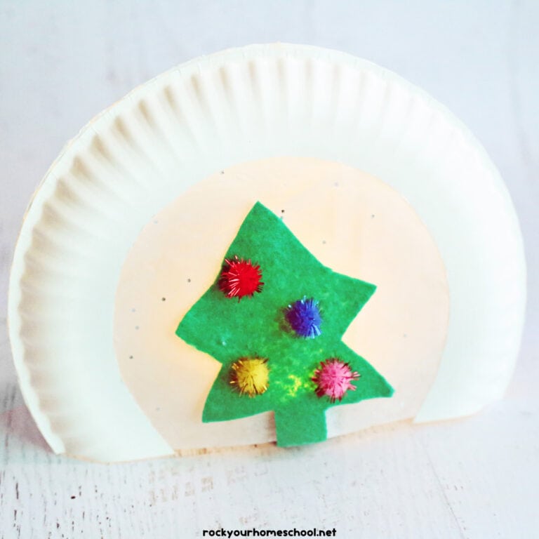 Christmas paper plate craft with green felt tree, pom poms, and light.