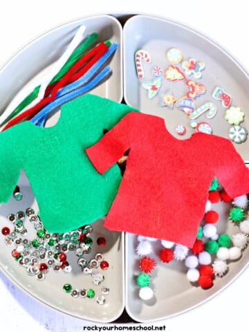 White tray with pipe cleaners, Christmas foam stickers, sequins, pom poms, and red and green felt sweater shapes.