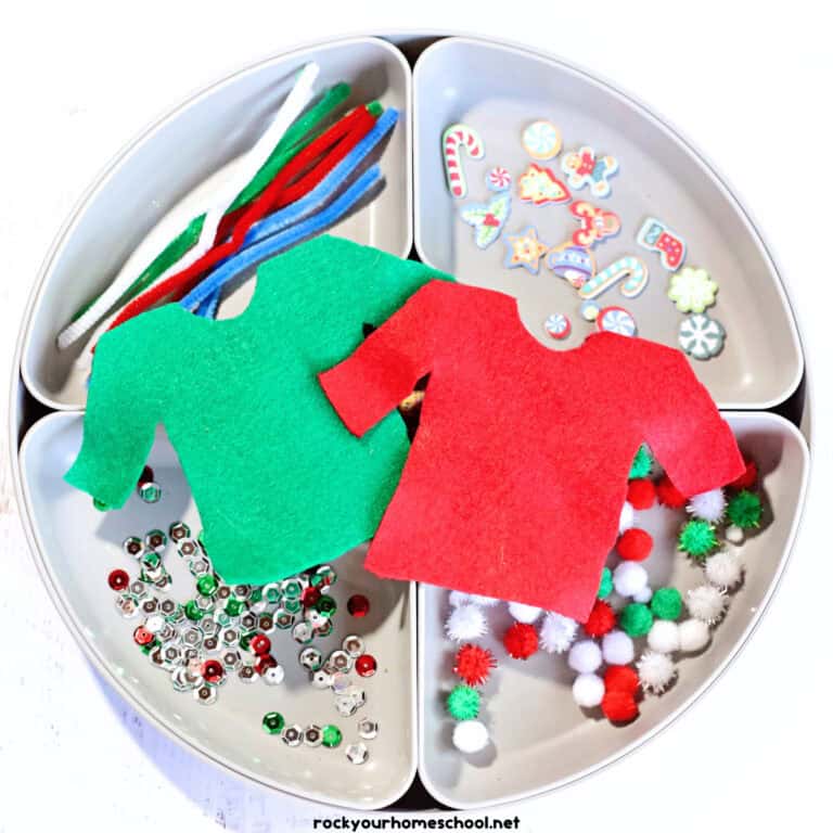 White tray with pipe cleaners, Christmas foam stickers, sequins, pom poms, and red and green felt sweater shapes.