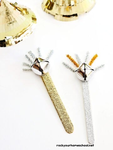 Two examples of popsicle stick noisemaker crafts for kids using gold and silver washi tape, jingle bells, and pipe cleaners.