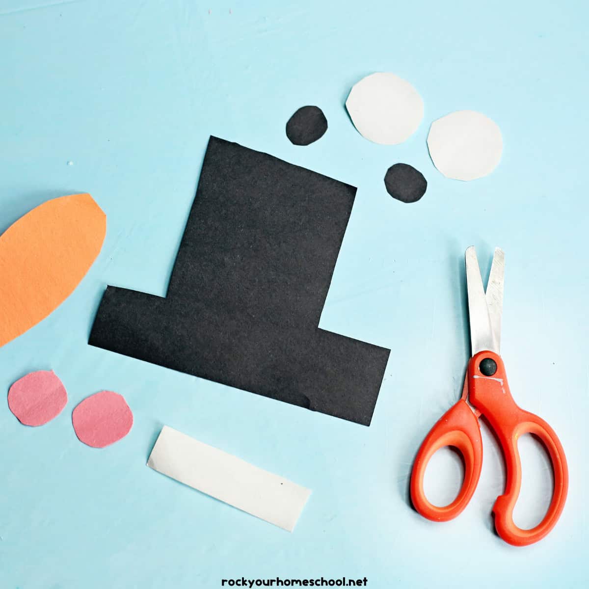 Scissors with construction paper pieces in hat, circles, and rectangle.