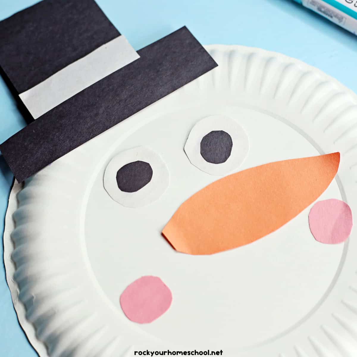 White paper plate with construction paper pieces of hat, eyes, nose, and pink cheeks.