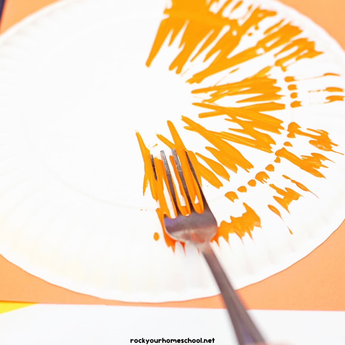 Back of white paper plate with fork and orange paint.