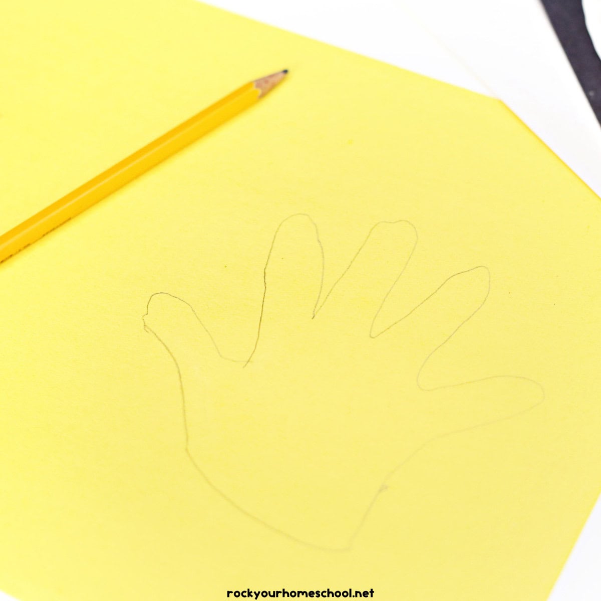 Yellow construction paper with pencil and tracing of child's hand.