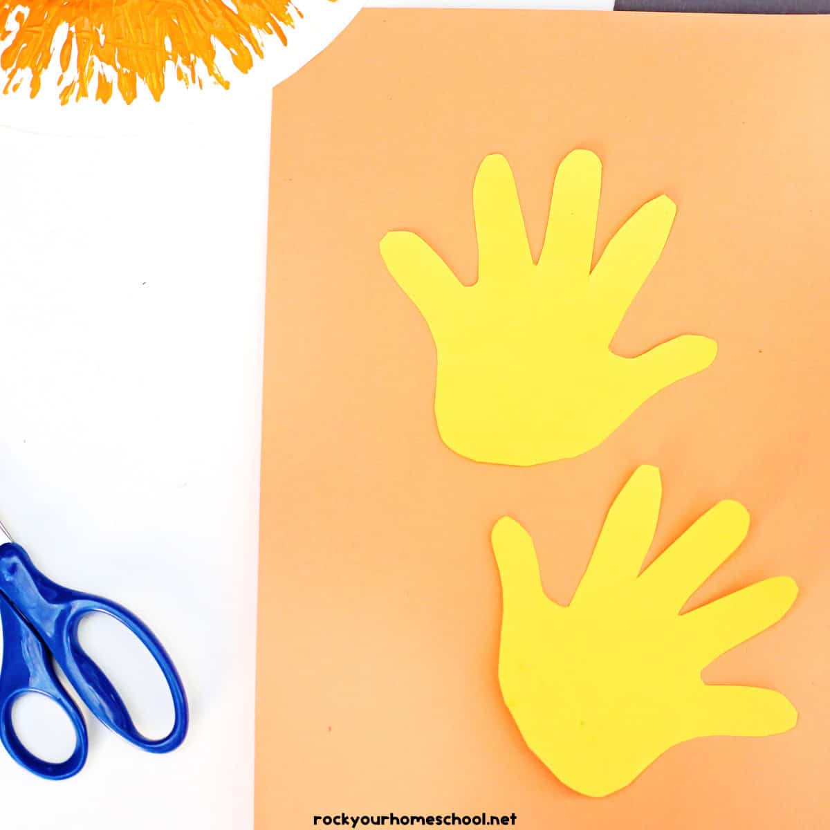 Two yellow handprints on orange paper with scissors.