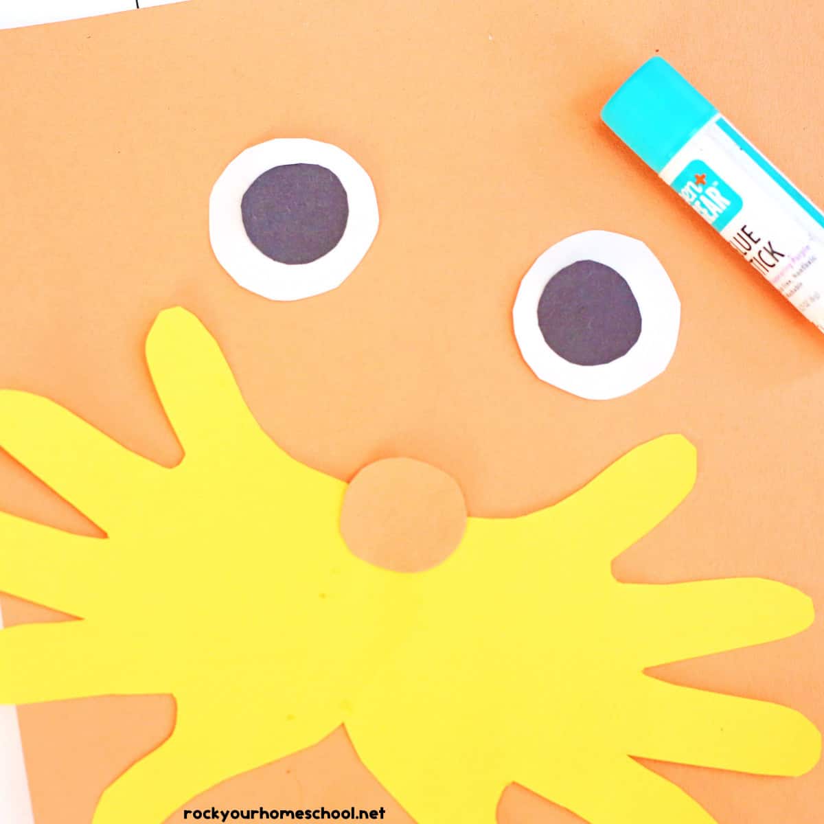 Glue stick, orange paper, paper eye balls, yellow mustache with orange circle nose.