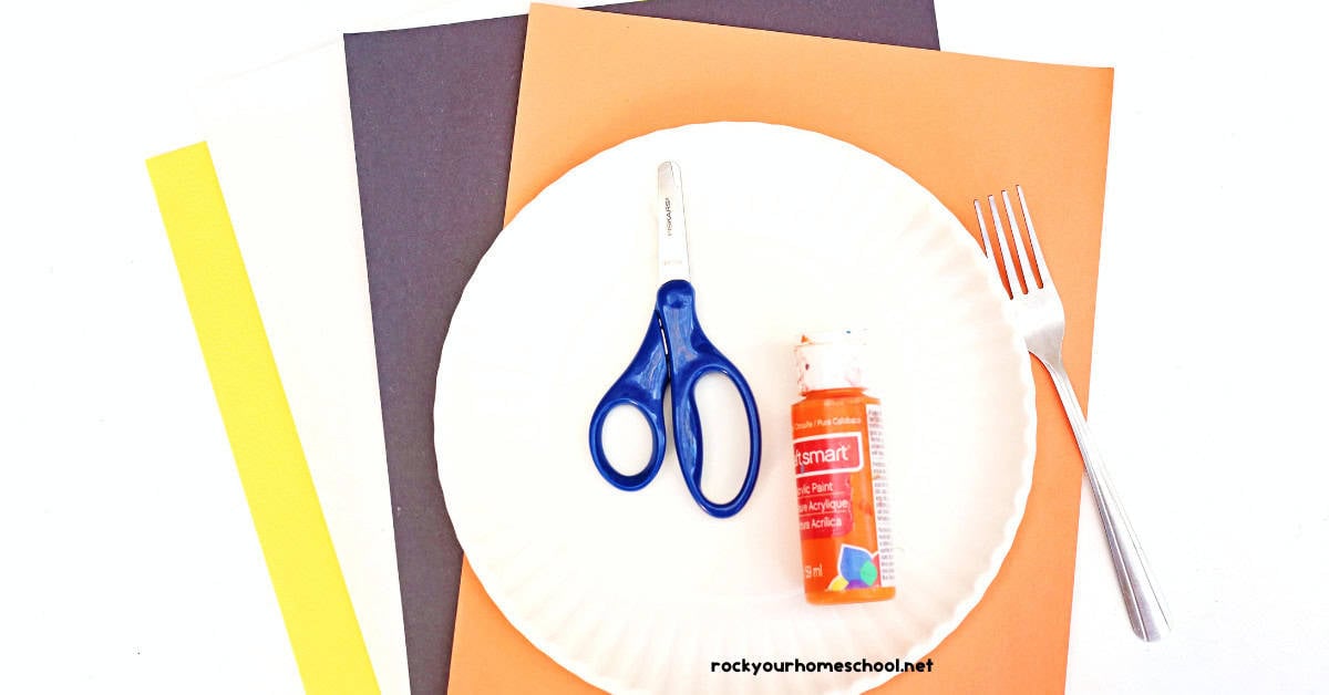 Construction paper in yellow, white, black, and orange with paper plates, scissors, orange paint, and fork.