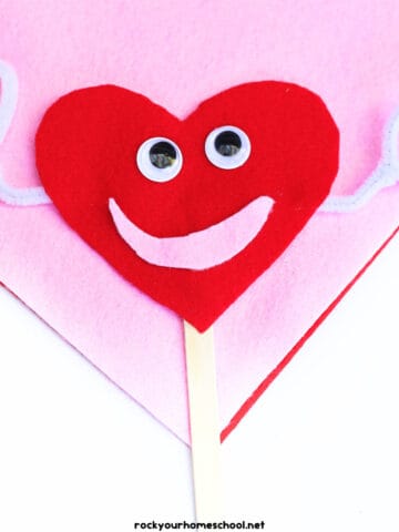 Example of felt heart craft for cute puppet in red and pink with white pipe cleaners, googly eyes, and popsicle stick.