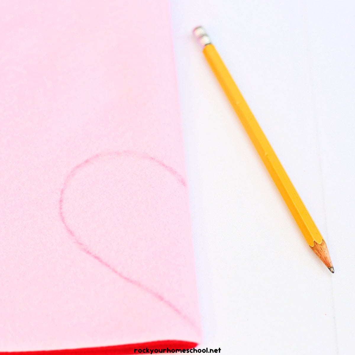 Pencil and pink felt with half of a heart shape.