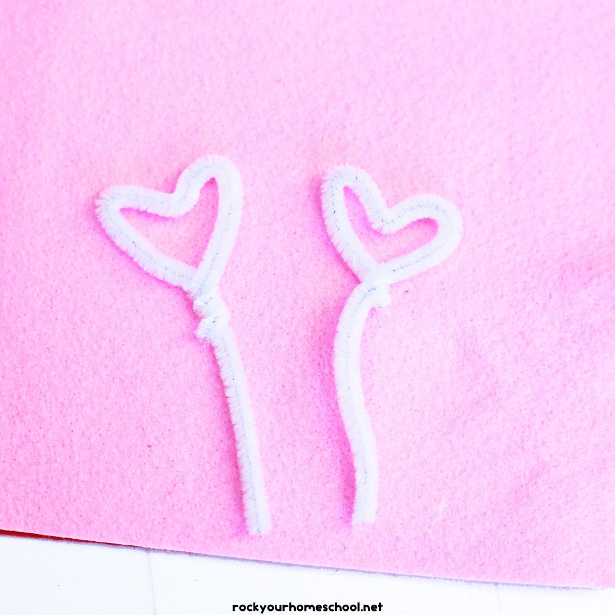 Two white pipe cleaners with small hearts on pink felt.