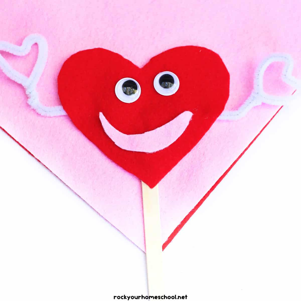 Example of felt heart craft for cute puppet in red and pink with white pipe cleaners, googly eyes, and popsicle stick.