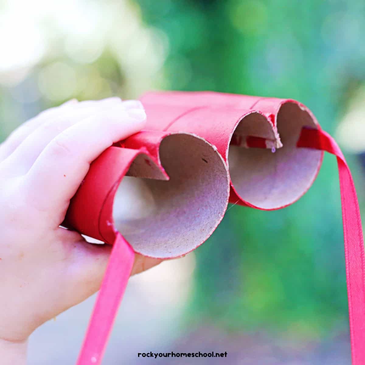 Child holding red heart-shaped toilet paper roll binoculars.