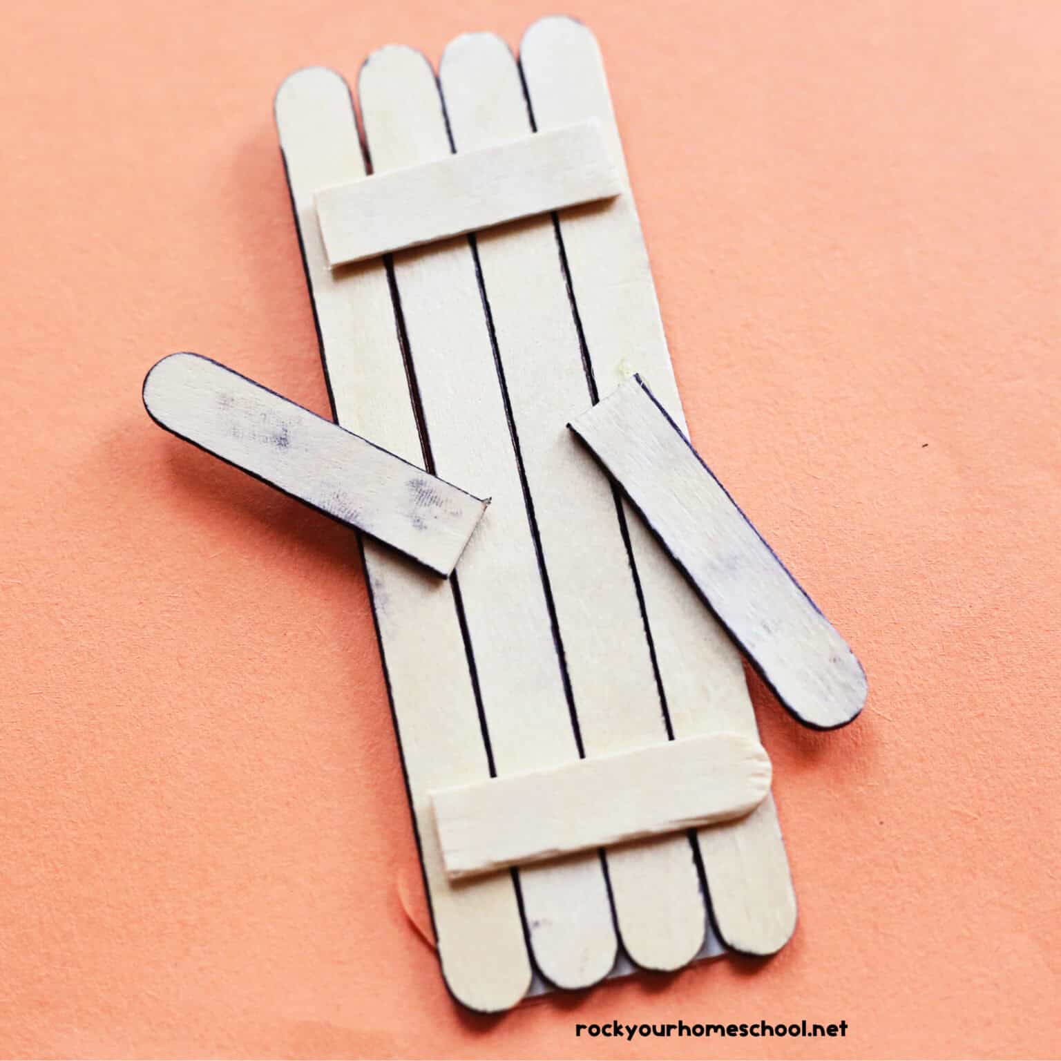 Back of popsicle stick penguin craft on orange paper.
