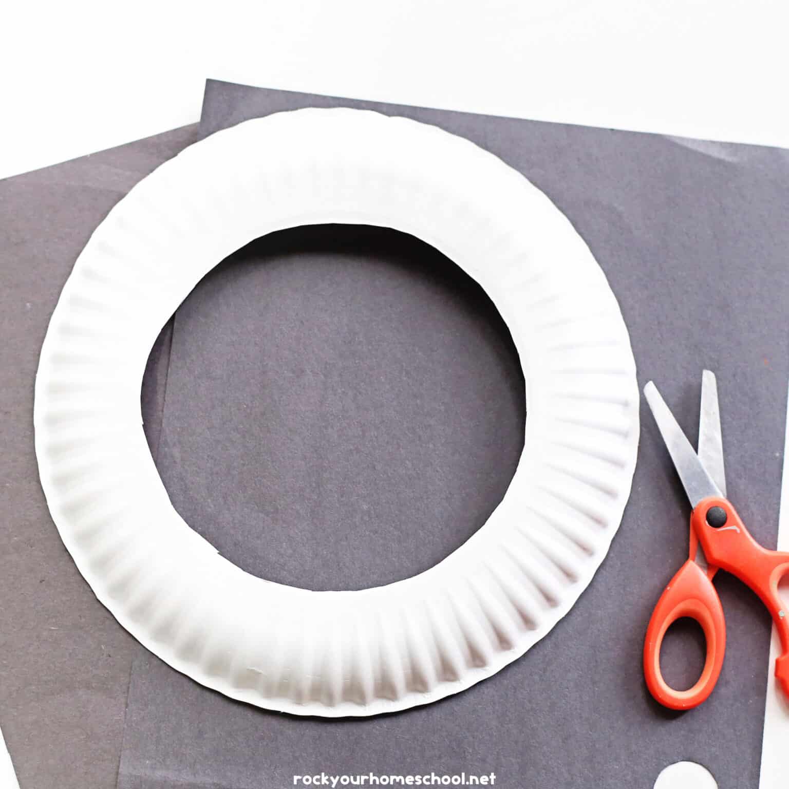 Black construction paper, scissors, and paper plate with center cut out.