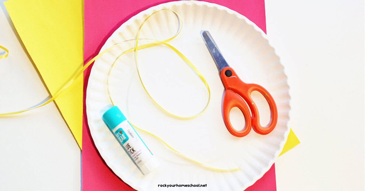 Paper plate, yellow ribbon, glue stick, scissors, and red and yellow construction paper.