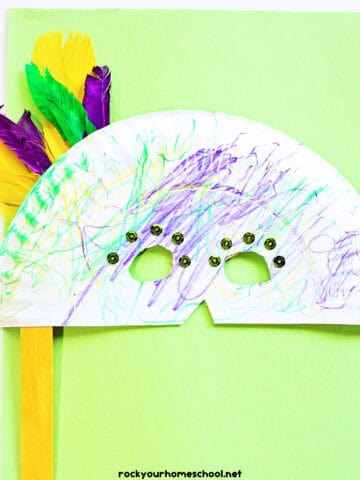 Example of paper plate Mardi Gras mask craft with yellow, purple, and green feathers and sequins.