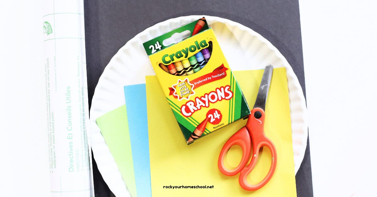 Black construction paper, scissors, contact paper roll, box of crayons and light green, light blue, and yellow paper.