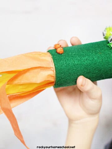 Young boy blowing through toilet paper roll dragon craft with tissue paper for a fire breathing effect.