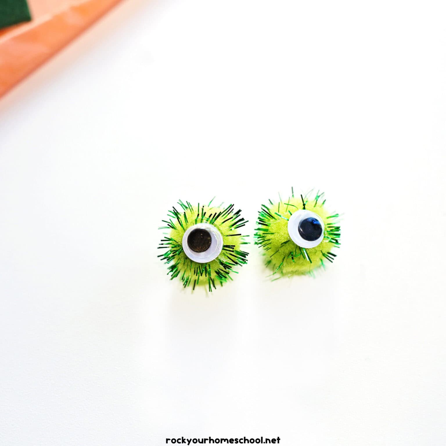 2 light green pom poms with googly eyes glued on.