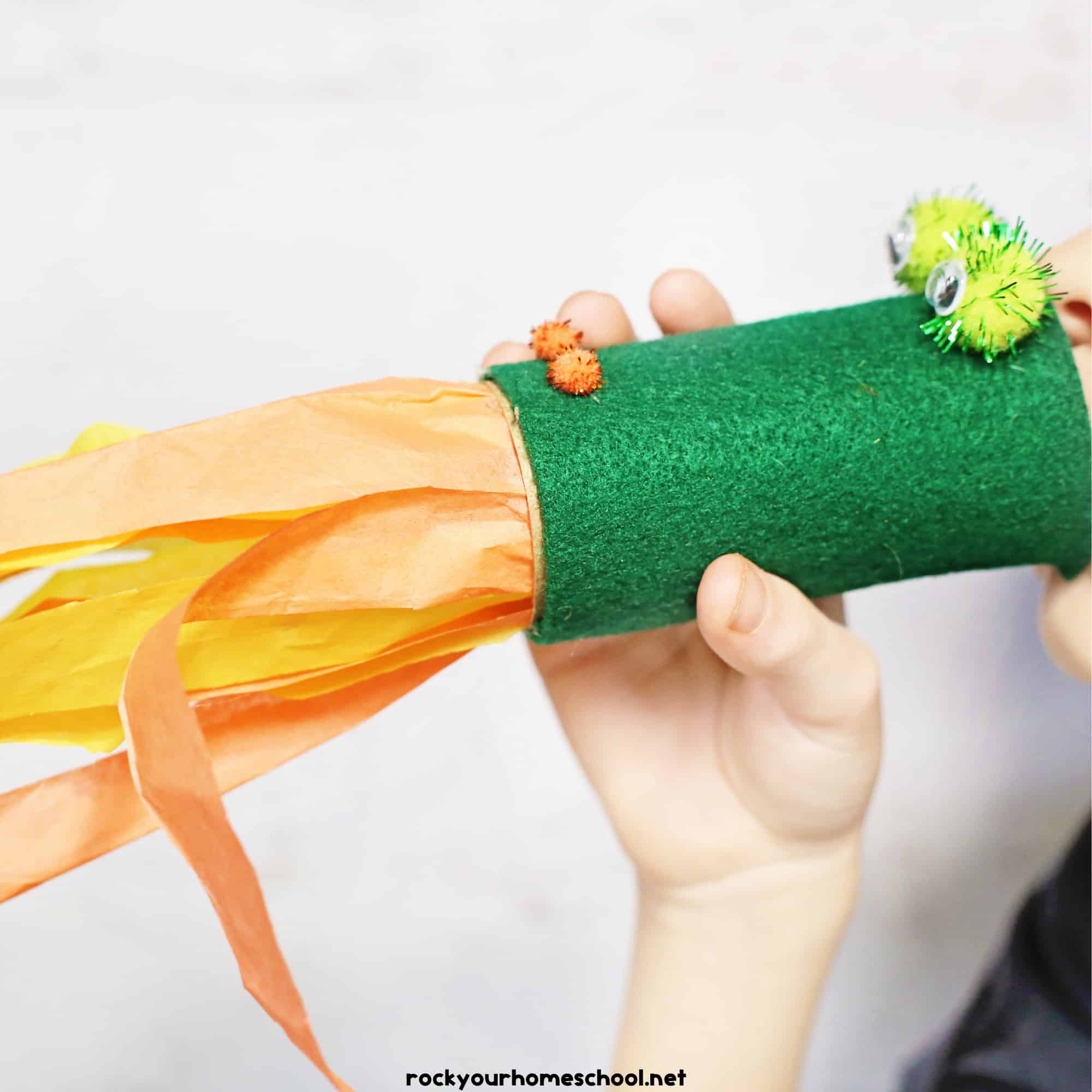 Young boy blowing through toilet paper roll dragon craft with tissue paper for a fire breathing effect.