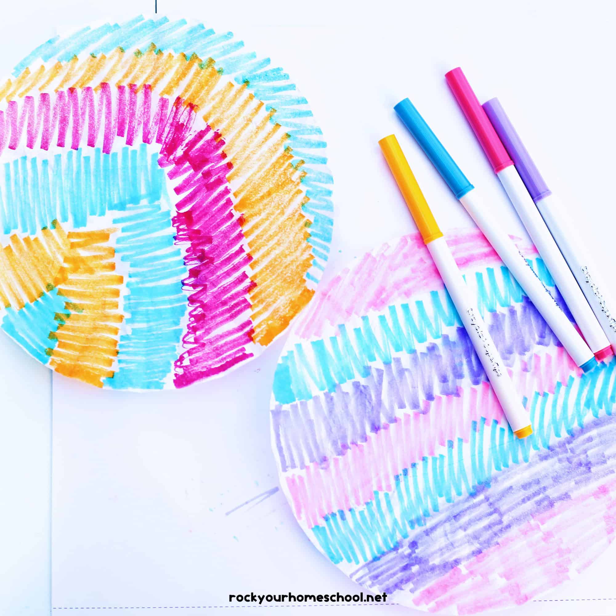 Two coffee filters colored with orange, blue, pink, and purple markers.