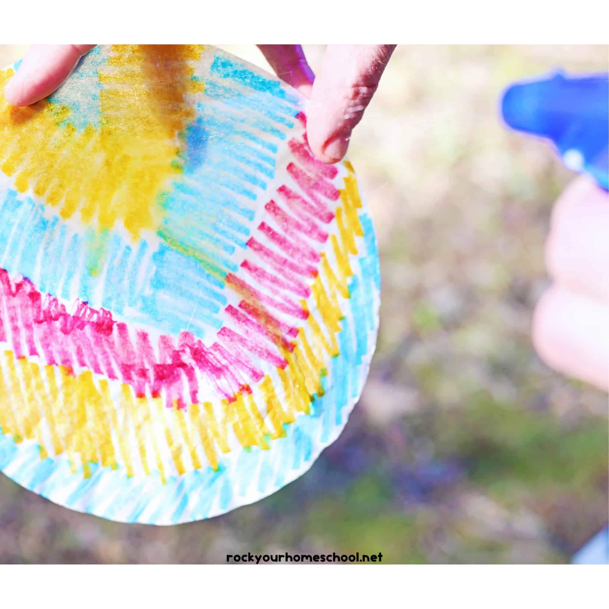 Child using blue spray bottle to spray water on coffee filter colored with markers.