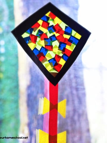 Kite suncatcher craft for kids featuring black diamond frame with red, yellow, and blue tissue paper squares with red paper string and yellow bows.