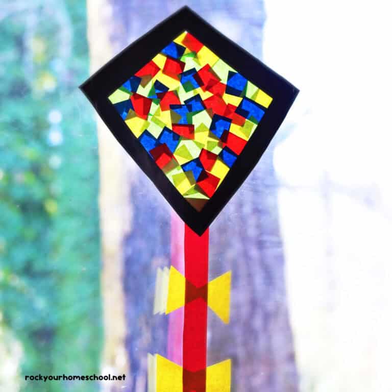 Kite suncatcher craft for kids featuring black diamond frame with red, yellow, and blue tissue paper squares with red paper string and yellow bows.