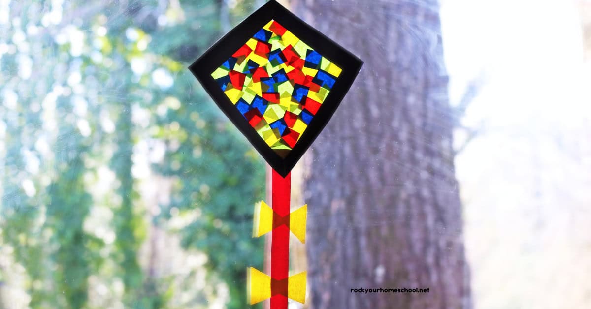 Example of kite suncatcher craft for kids made with black construction paper and red, blue, and yellow paper squares.