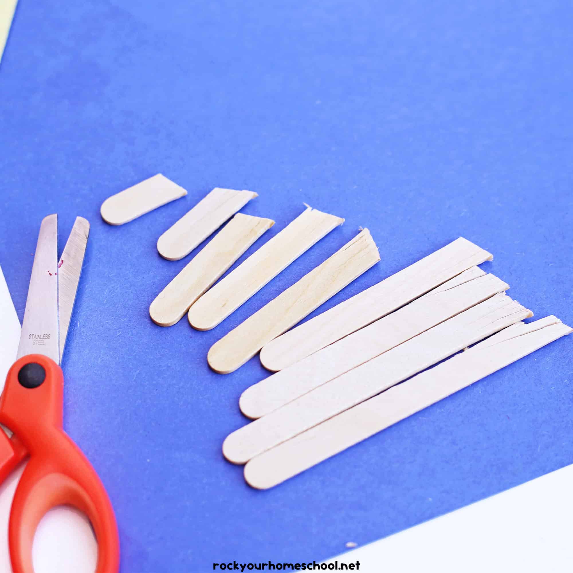 Cut popsicle sticks on blue construction paper with scissors.